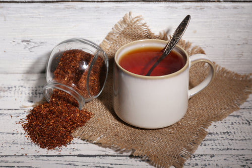 A cup of tasty rooibos tea sits on an old white wooden table.