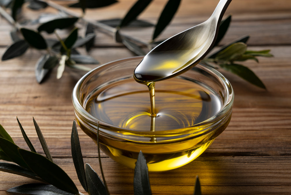 Spooning olive oil into a bowl placed on a wooden background