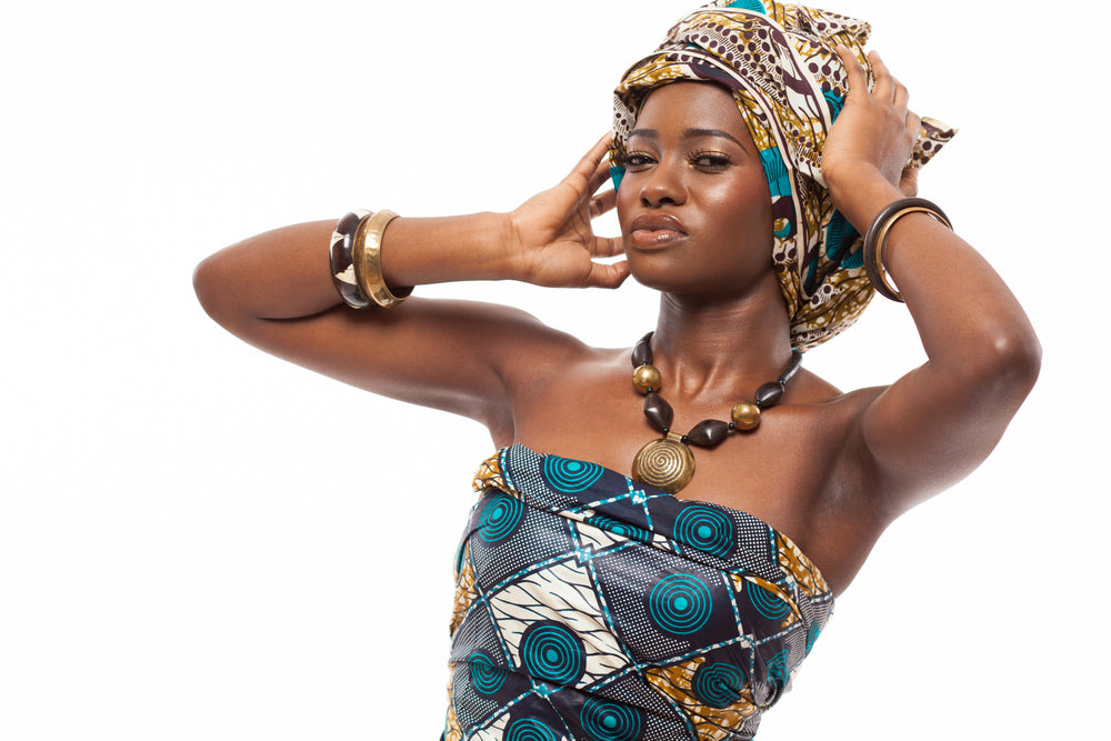 An African woman wearing a vibrant Ankara print dress with rich colors and patterns. She accessorizes with traditional African jewelry.