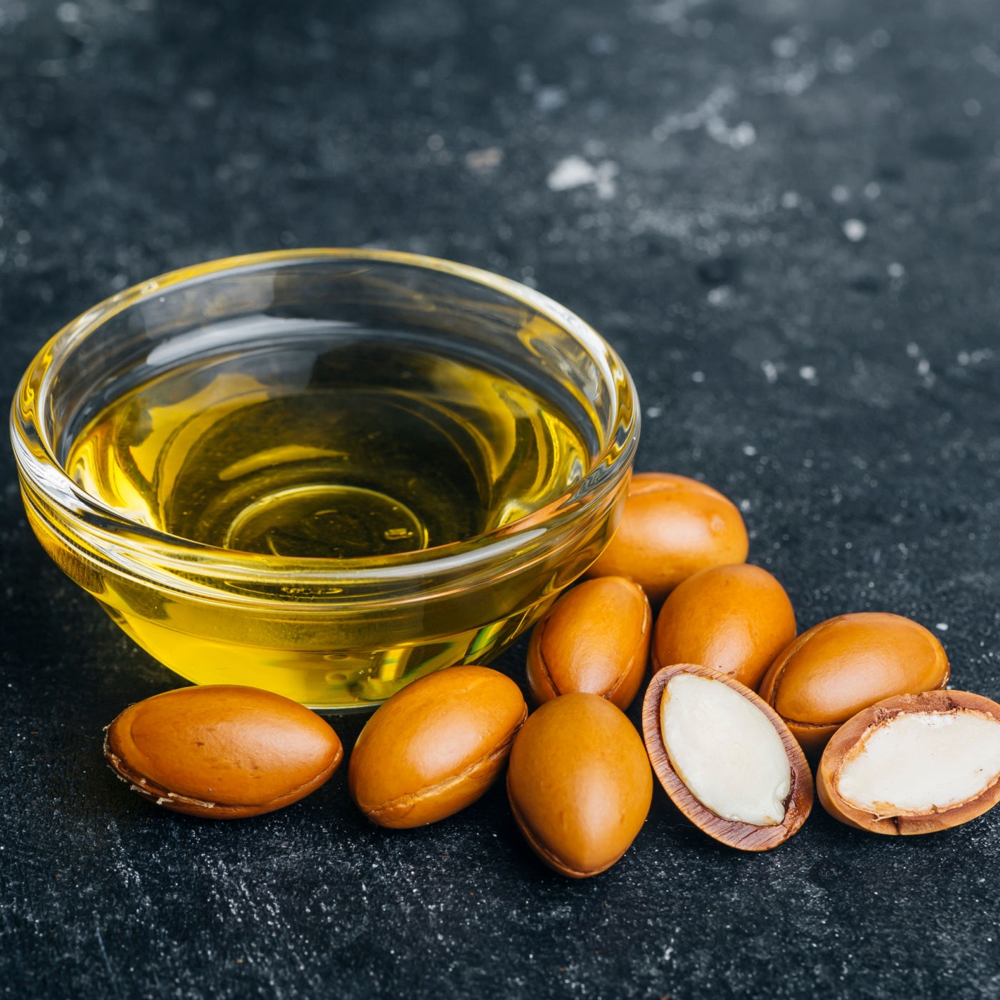 Argan seeds and oil on a dark wooden background.