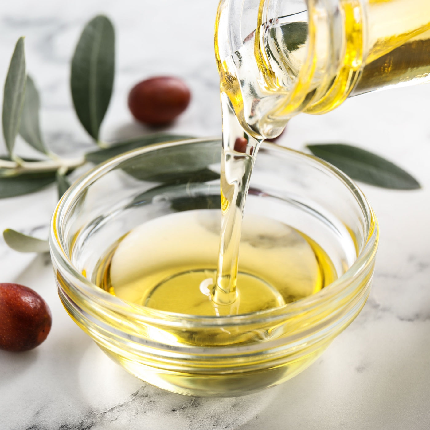 Pouring with jojoba oil from jug into bowl on white marble table